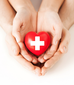 Parent and Child's hands placed under another with a heart shaped object in the child hand.
