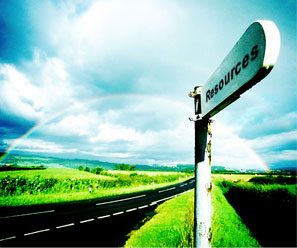 Road sign that says Resources on it. There is a rainbow in the background going over a field.
